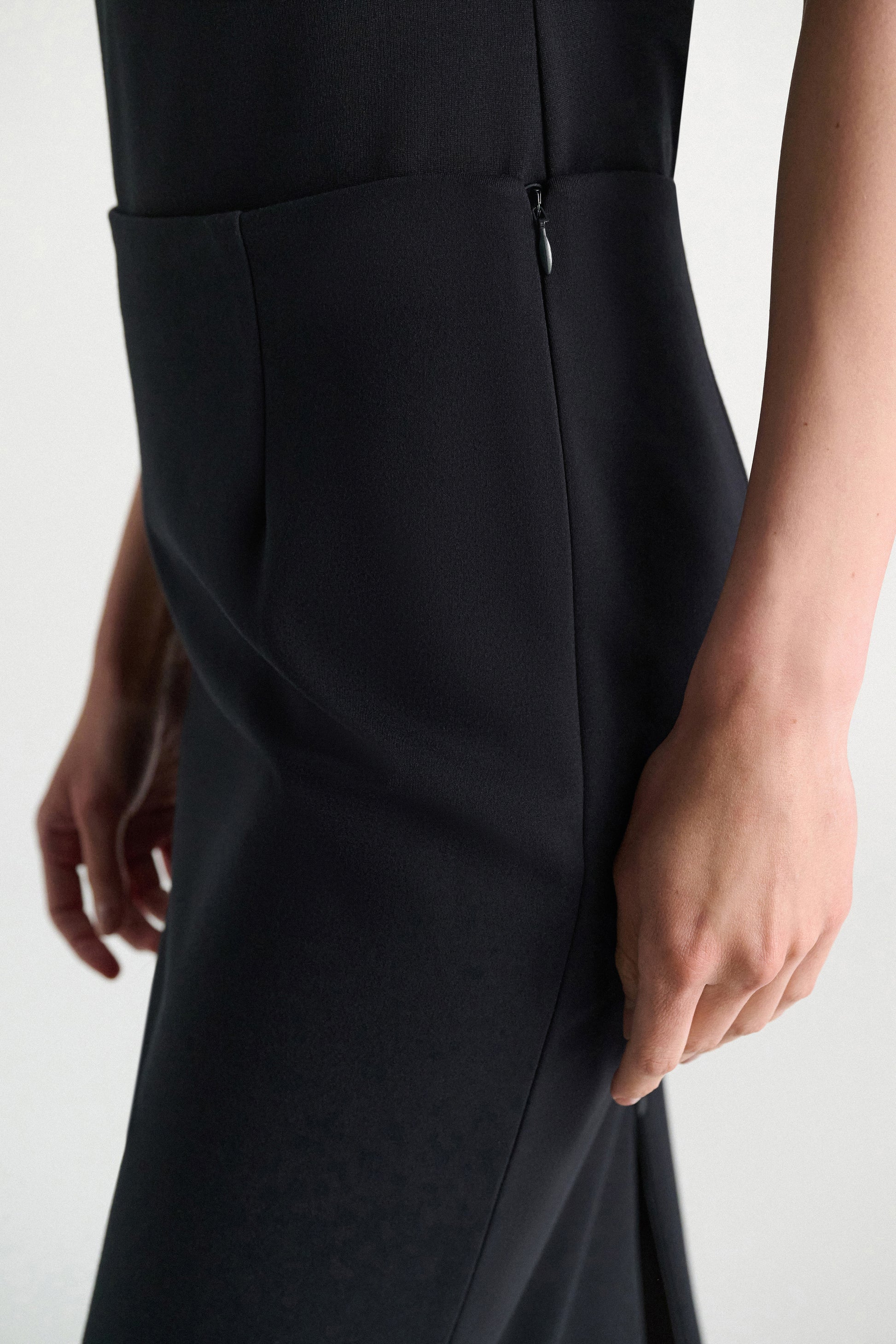 A close-up side view of a person wearing the Dorothee Schumacher Emotional Essence Skirt—a black pencil skirt with a side zipper, crafted from smooth Punto Milano fabric, and styled as an elegant work week essential.