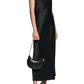 A woman wears the Sense of Shine Dress by Dorothee Schumacher, a stretch silk-satin midi with adjustable spaghetti straps, paired with black strappy heeled sandals and a small black handbag.