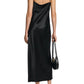 A person shown from the back wears the Dorothee Schumacher Sense of Shine Dress, a black stretch silk-satin slip with thin straps and a waterfall neckline, paired with black heeled sandals and a small black handbag.