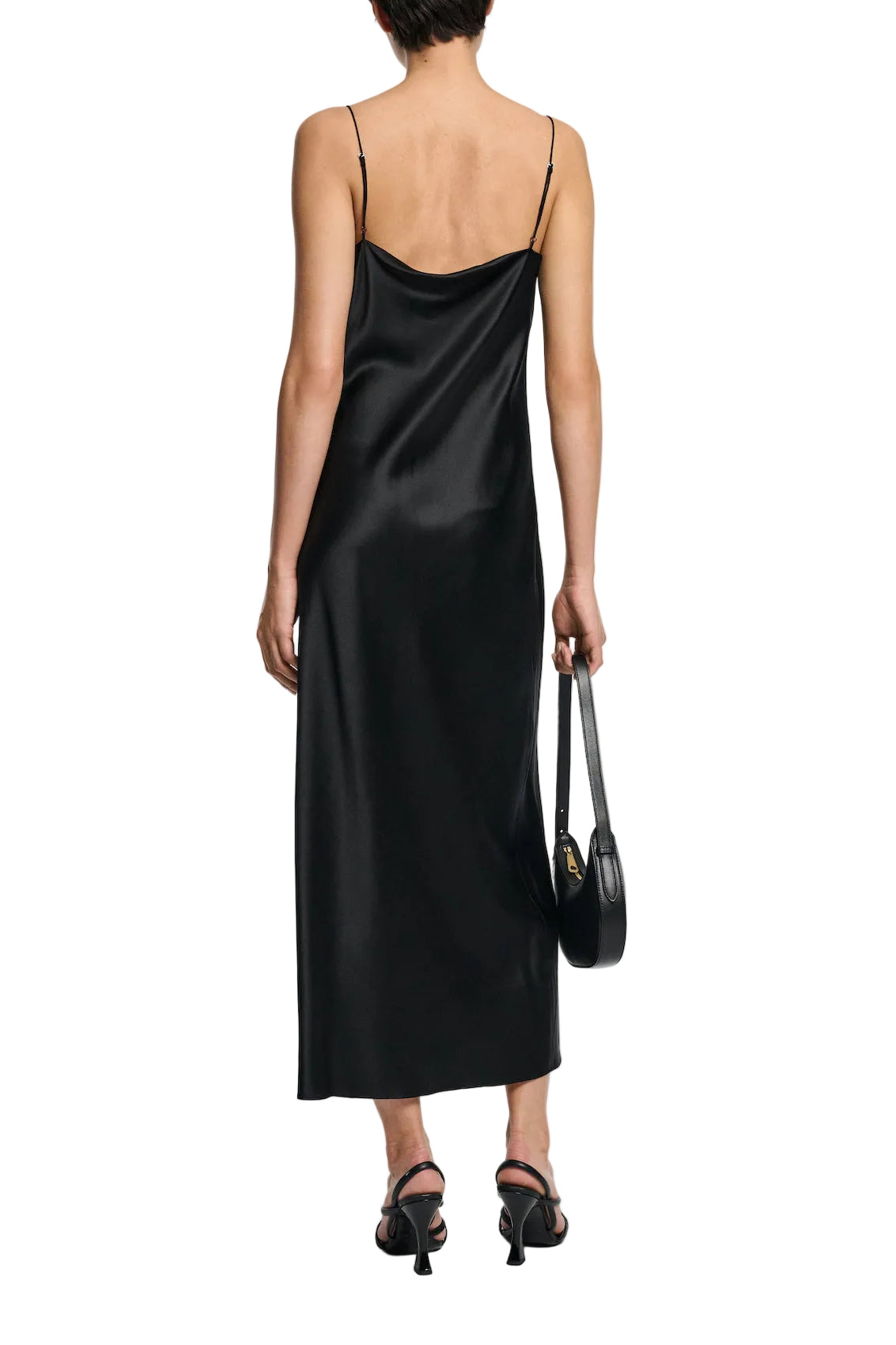A person shown from the back wears the Dorothee Schumacher Sense of Shine Dress, a black stretch silk-satin slip with thin straps and a waterfall neckline, paired with black heeled sandals and a small black handbag.