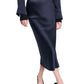 A person wearing the Dorothee Schumacher Sense of Shine Skirt in dark navy stretch silk-satin with an elastic waistband, a matching long-sleeve shirt, a black belt with gold accents, and black pointed-toe slingback heels.