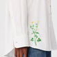 A person wearing the Stella McCartney Flower Embroidered Shirt with yellow floral designs near the hem, paired with blue jeans.