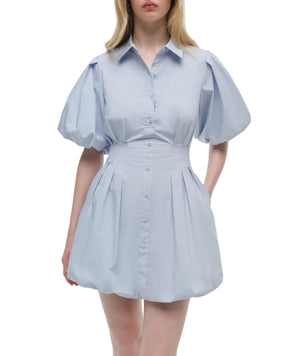A woman wears the Cleo Dress by Simkhai, a light blue cotton mini with button-down front, balloon sleeves, and pleated skirt, reminiscent of a periwinkle sky.