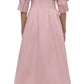 Rear view of a person wearing the Simkhai Signature Jazz Dress, a long pink cotton poplin creation with an A-line silhouette and rolled sleeves, paired with beige heels against a white background.