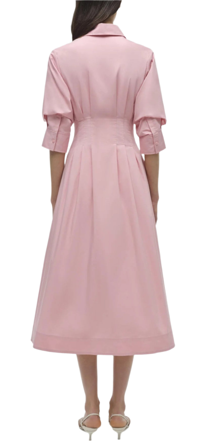 Rear view of a person wearing the Simkhai Signature Jazz Dress, a long pink cotton poplin creation with an A-line silhouette and rolled sleeves, paired with beige heels against a white background.