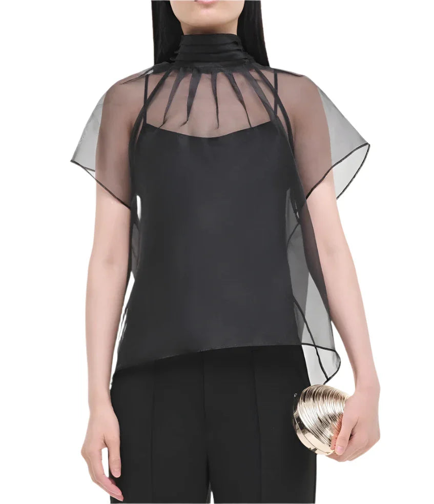 A person elegantly holding a gold clutch while wearing the Simkhai Feyre Top, which features a black sheer design with short sleeves and a high collar.