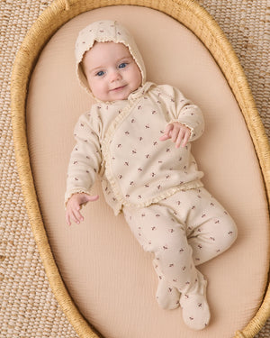 A newborn baby in the Quincy Mae Baby Girls’ Take Home Set, made from cream-colored waffle knit fabric with delicate patterns, lies on a beige mattress in a woven basket, gazing up with a gentle smile—an ideal choice for a cozy first outfit or a newborn coming home ensemble.