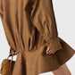A person holds a small quilted brown handbag, wearing a Stella McCartney Washed Cotton Peplum Shirt Dress. Only the lower half of the dress and their hand are visible.
