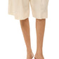 A person stands against a plain white background wearing beige knee-length shorts and stylish yellow Brigitte Raffia Mules by Staud.