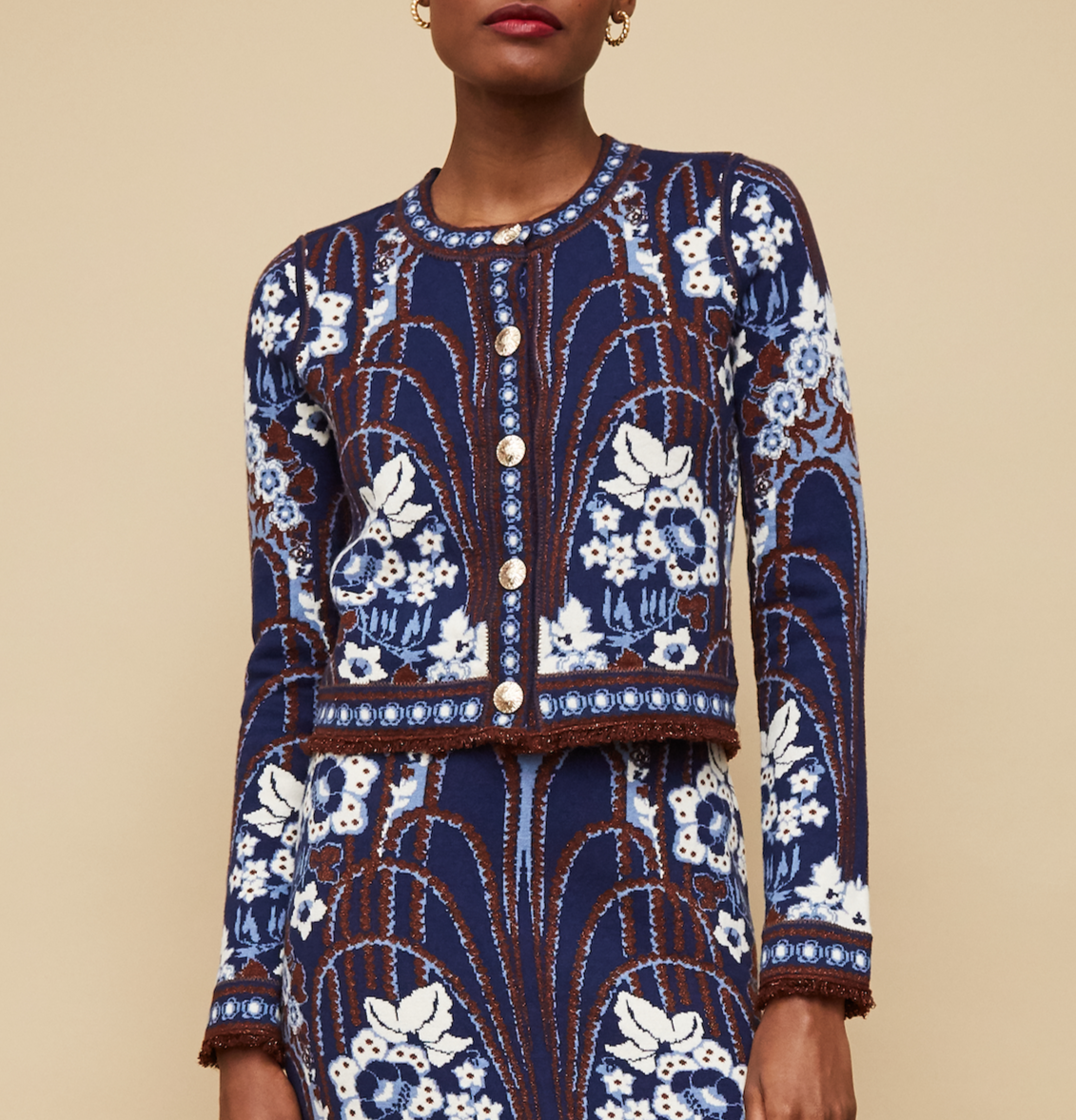 A woman wearing the Cara Cara Livi Jacket, a blue jacquard knit cardigan with white and brown floral designs, stands against a beige background.