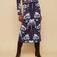 A person models the Cara Cara Clara Skirt and matching blue jacquard jacket with white floral patterns, paired with dark brown knee-high boots, against a beige background.