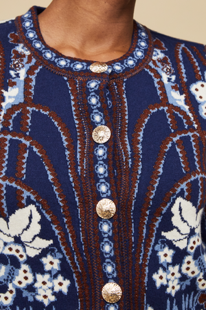 Close-up of the Cara Cara Livi Jacket, a blue jacquard knit cardigan featuring white and brown floral patterns, silver decorative buttons, and subtle fringe detail.