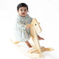 A baby wearing the Angel Dear Baby Girls' Long Sleeve Petal Collar Dress and Bloomer sits on a light wooden rocking horse against a white background.