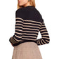 A person, turned slightly to the side, is wearing the Cara Cara Finnegan Jacket, a black and white striped piece with a boxy fit by Cara Cara, paired perfectly with a plaid skirt.