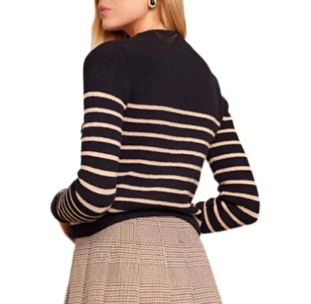 A person, turned slightly to the side, is wearing the Cara Cara Finnegan Jacket, a black and white striped piece with a boxy fit by Cara Cara, paired perfectly with a plaid skirt.