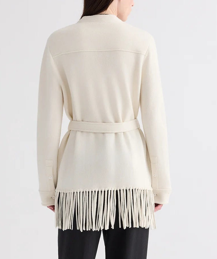A person is seen from the back against a plain background, wearing the TWP Thea Italian Cashmere Jacket—an off-white piece featuring a belted waist and fringe trim along the hem.