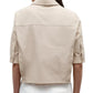 A person wearing the TWP Short Lived Top—a light beige, boxy fit short-sleeve collared shirt with buttoned cuffs—viewed from the back and paired with white pants.
