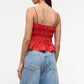 A woman seen from the back wears the Staud Ayla Linen Tank, a red cami with thin straps and a smocked bodice, paired with blue high-waisted jeans.
