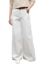 Model wears TWP’s Dee's Linen Trouser—wide-leg, white cotton linen—paired with a beige shirt, brown belt, and white shoes, one hand in the pocket, set against a white backdrop.