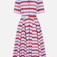 The Mella Bayadere Stripe Dress by Emilia Wickstead is a knee-length cotton shirt dress with short sleeves, a collared neckline, a belted waist, and a button-down front. Featuring horizontal red, white, and light blue stripes, this classic summer dress offers effortless style.