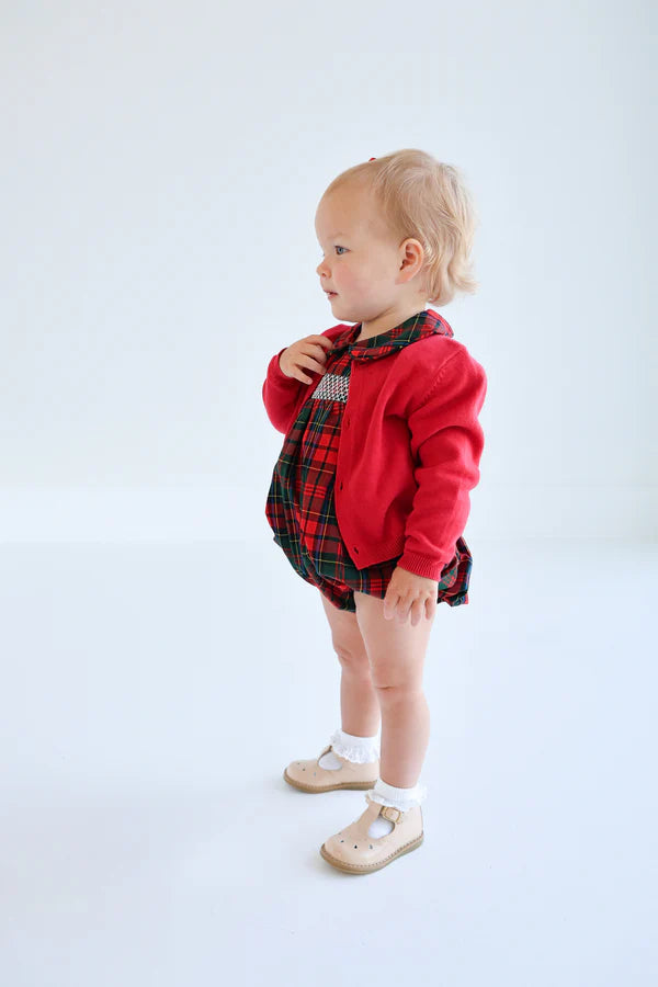 A toddler in The Beaufort Bonnet Company's Baby Girls' Dottie Hart Bubble stands against a plain white background, looking to the side.