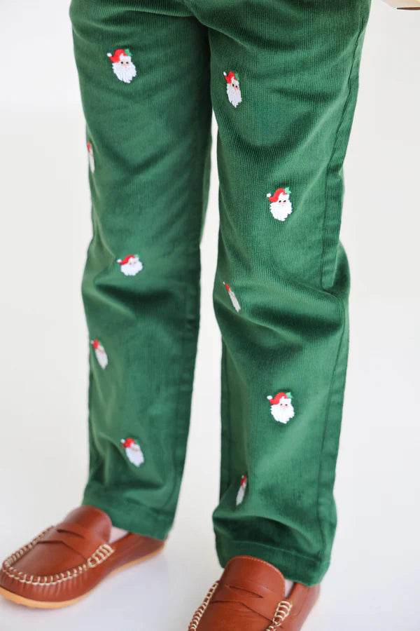 A child models The Beaufort Bonnet Company Boys' Critter Prep School Corduroy Pant—green pants with small embroidered Santas—paired with brown moccasin-style shoes, standing against a plain background.