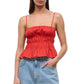 A woman wears the Staud Ayla Linen Tank—a red, sleeveless peplum top with a smocked bodice and spaghetti straps—paired with light blue high-waisted jeans for a chic, cropped look.