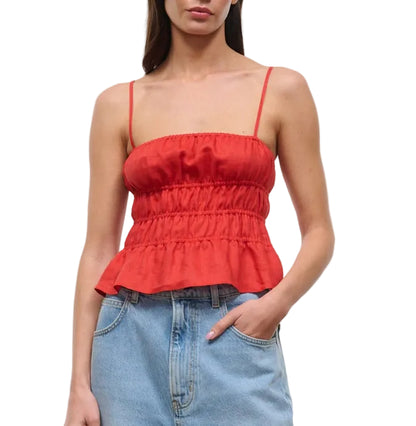 A woman wears the Staud Ayla Linen Tank—a red, sleeveless peplum top with a smocked bodice and spaghetti straps—paired with light blue high-waisted jeans for a chic, cropped look.