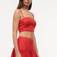 A person wearing the Staud Federico Linen Tank—a sleeveless red crop top—paired with a matching high-waisted, flared skirt stands against a plain white background.