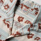 A close-up of the Faherty Breeze Camp Shirt, a light blue and cream button-up featuring brown floral patterns and two visible brand labels on the collar.