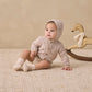 A baby wearing Quincy Mae’s Baby Girls’ Gathered Bloomer with elasticated leg openings sits on a textured rug next to a wooden rocking horse, paired with a knit hooded sweater and socks.