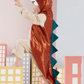 A child in a Meri Meri Dinosaur Costume, featuring spikes and a hooded jacket, appears to be playfully roaring, standing among cardboard cutout buildings.