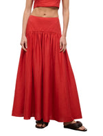 A person wearing the Staud Procida Linen Skirt in red—a high-waisted, ankle-length maxi with a gathered waistband—paired with black sandals. Their arms are relaxed by their sides.
