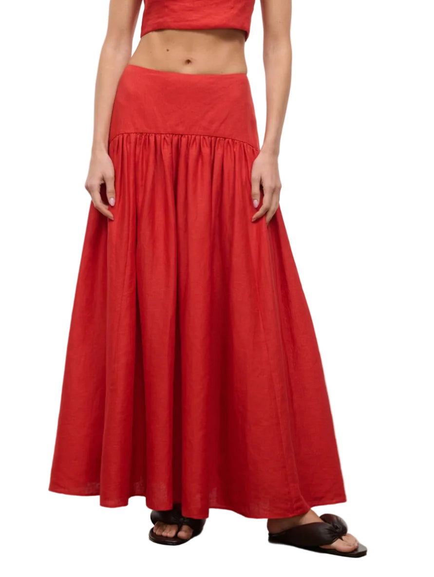 A person wearing the Staud Procida Linen Skirt in red—a high-waisted, ankle-length maxi with a gathered waistband—paired with black sandals. Their arms are relaxed by their sides.