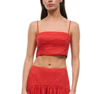 A woman wearing the Staud Federico Linen Tank—a red sleeveless crop top with spaghetti straps—paired with a matching high-waisted skirt, stands against a white background.