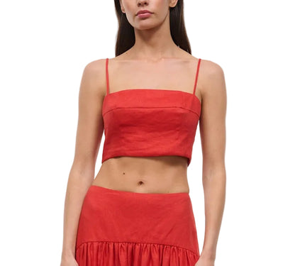 A woman wearing the Staud Federico Linen Tank—a red sleeveless crop top with spaghetti straps—paired with a matching high-waisted skirt, stands against a white background.