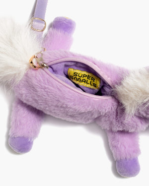 The Opal Plush Unicorn Bag by Super Smalls is a small purple animal-shaped purse with a zippered opening that reveals a yellow tag labeled “SUPER SMALLS” inside.
