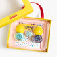 A yellow box holds the Super Smalls Paint It Mermaid Mini Nail Kit, featuring two yellow-capped bottles of peel-off nail polish, a seashell-shaped item, a blue container, and a sheet of shell nail stickers.