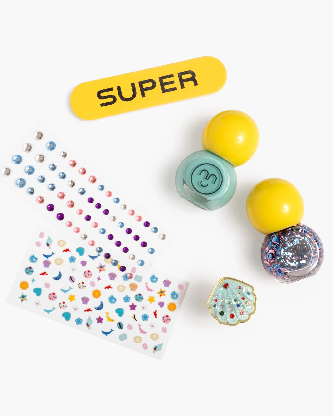 The Paint It Mermaid Mini Nail Kit by Super Smalls includes a yellow "SUPER" nail file, two shell nail sticker sheets, two gumball capsules, a teal container, and a seashell ring—your perfect mini mermaid manicure set.