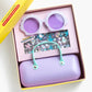 The Super Smalls Mermaid Splash & Sparkle Gemify Sunglasses & Case comes in a yellow box with purple mermaid sunglasses, a lavender purse with mint handle, and colorful mermaid-themed stickers—perfect for kids’ crafting fun.