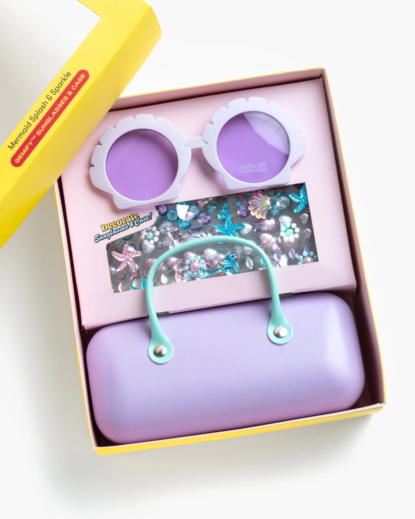 The Super Smalls Mermaid Splash & Sparkle Gemify Sunglasses & Case comes in a yellow box with purple mermaid sunglasses, a lavender purse with mint handle, and colorful mermaid-themed stickers—perfect for kids’ crafting fun.