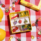 The Make It Fruity Mini Bead Kit by Super Smalls, featuring berry-bright beads, fruit charms, and string, is displayed on a red-and-white checkered surface next to lemons.