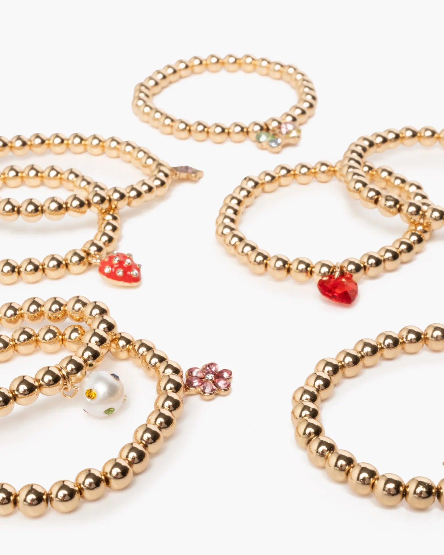 The Super Stack Bracelet Set by Super Smalls features gold beaded bracelets with heart, flower, and strawberry charms—an ideal mix-and-match accessory set for everyday wear, shown arranged on a white background.