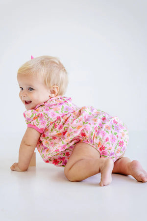 A blonde baby girl crawls on a white floor, smiling over her shoulder while wearing The Beaufort Bonnet Company's Baby Girls' Pima Ramona Ruffle Bubble.