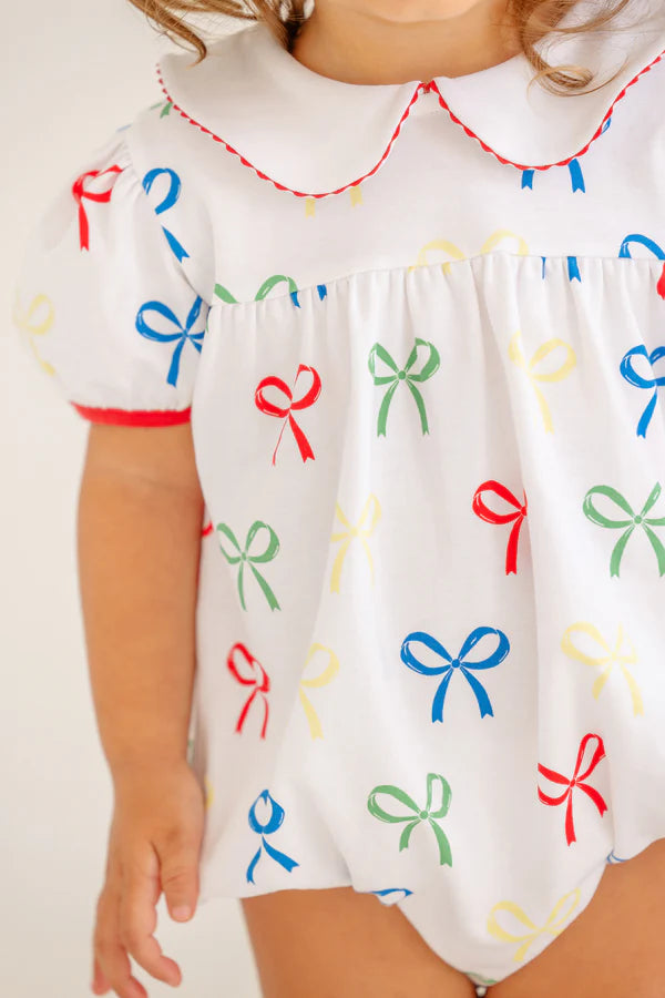 The Beaufort Bonnet Company’s Baby Girls' Cindy Lou Bubble features puffed sleeves, a scalloped collar, and a colorful bow pattern in red, green, yellow, and blue—a delightful addition to any little girl's wardrobe.
