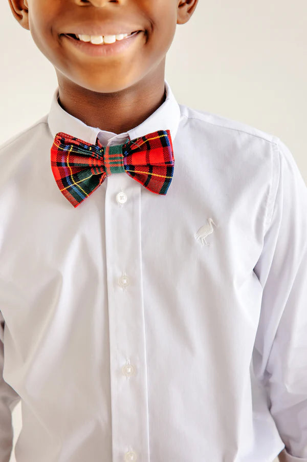 A young person wears a white dress shirt with The Beaufort Bonnet Company’s Baylor Bowtie in Paces Mill Plaid, a pre-tied adjustable bow tie with a subtle embroidered logo on the chest, smiling.