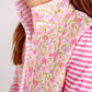 A girl wears The Beaufort Bonnet Company's Baby Girls' and Girl's Vaughn Vest in the Grand Cayman Gardens floral pattern over a pink and white striped shirt.