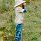 Dressed in the Great Pretenders Forest Guardian Set with Accessories, a child wearing a safari hat and casual clothes stands in grassy outdoors, holding binoculars and gazing into the distance—perfectly embodying the adventurous spirit of a young park ranger.