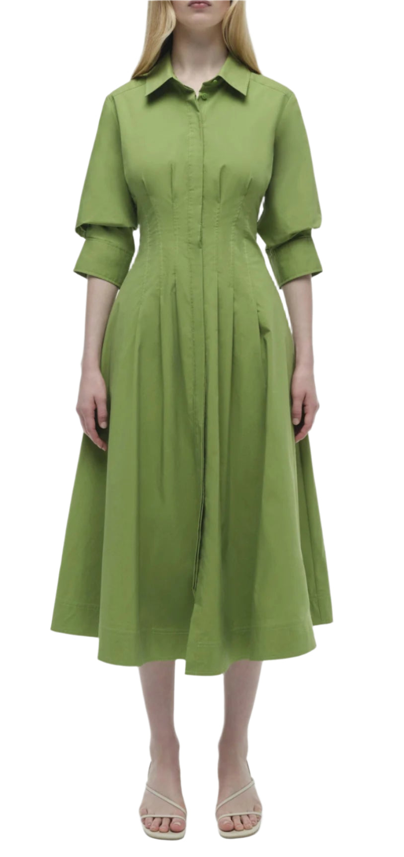 A person stands against a white background wearing the Simkhai Signature Jazz Dress, featuring a green A-line silhouette, knee-length with long sleeves, paired with beige sandals.