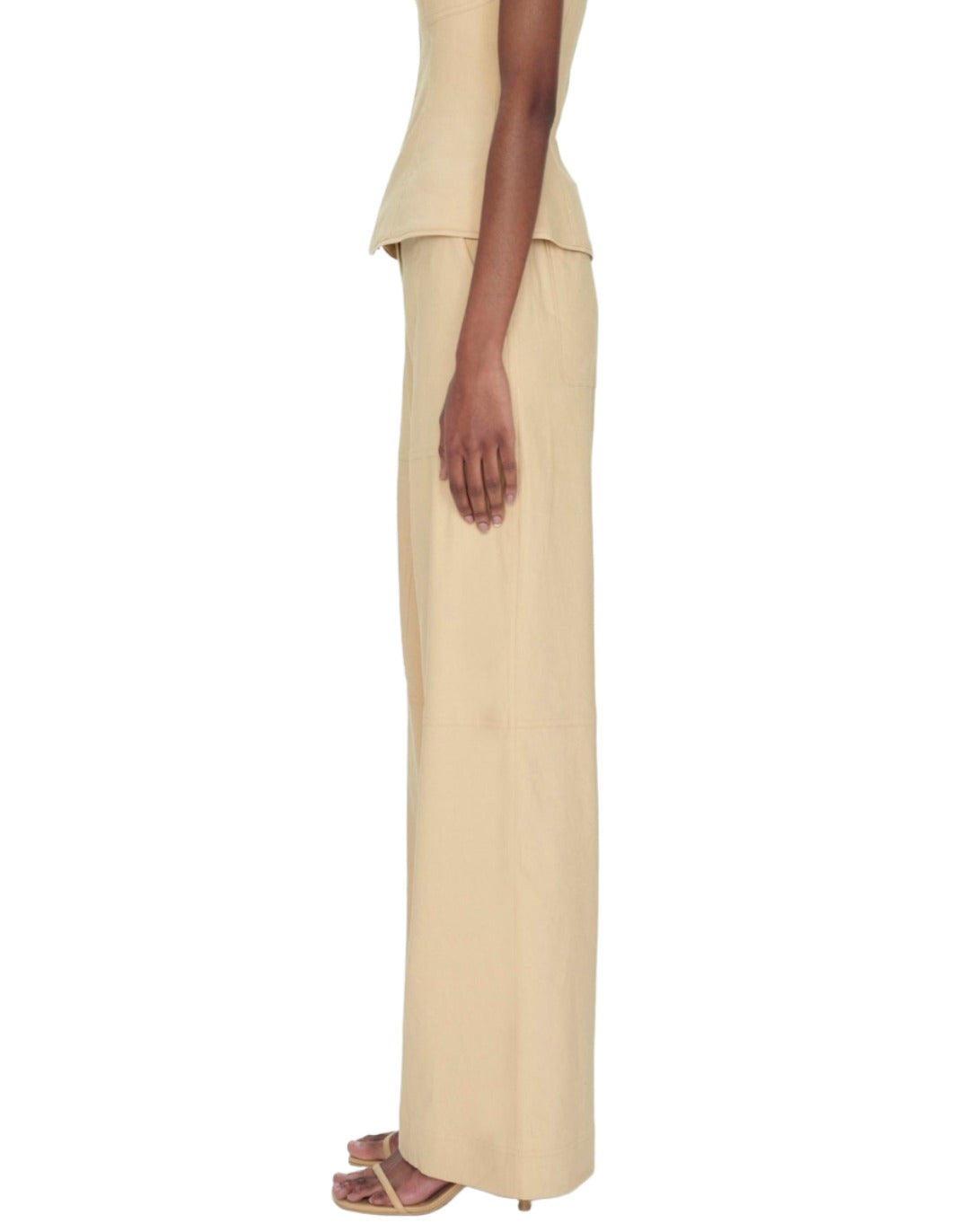 Side view of a woman wearing a cream peplum top and matching Simkhai Amaya Belted Linen Pants, with one hand slightly visible along her seam.